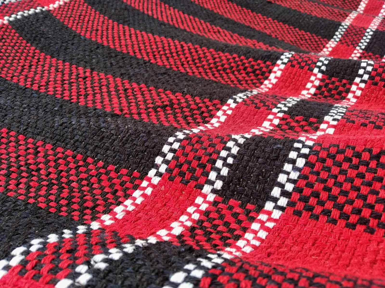 A close-up of a red, black and white tartan weave, its checks crossing diagonally across the frame.